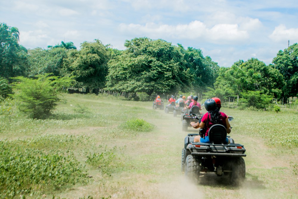 Convoy de ATVs recorriendo campo abierto con palmeras durante tour en Puerto Plata