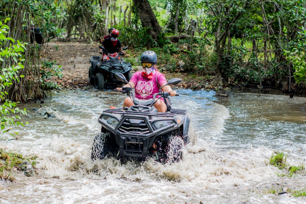 ATV negro cargado de turistas cruzando un riachuelo tropical en Maimón